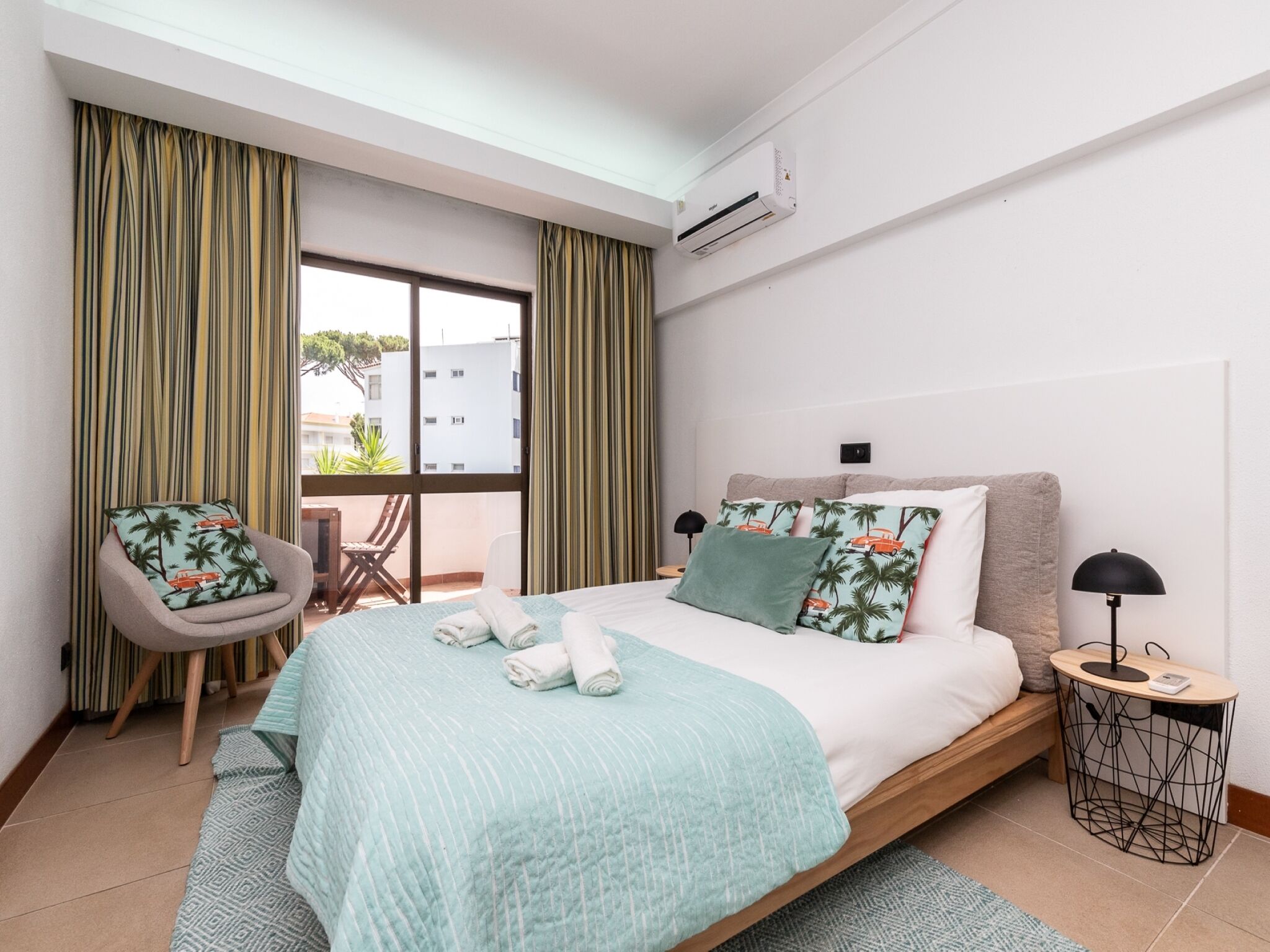 Quarto de hotel com cama, cadeira, mesa pequena e ar condicionado.