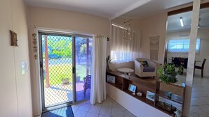 A living room with a sliding glass door leading to a patio, a sofa, a small table, and a decorative plant. - Perfect location close to beach's, town centre and the golf course (South West Rocks)