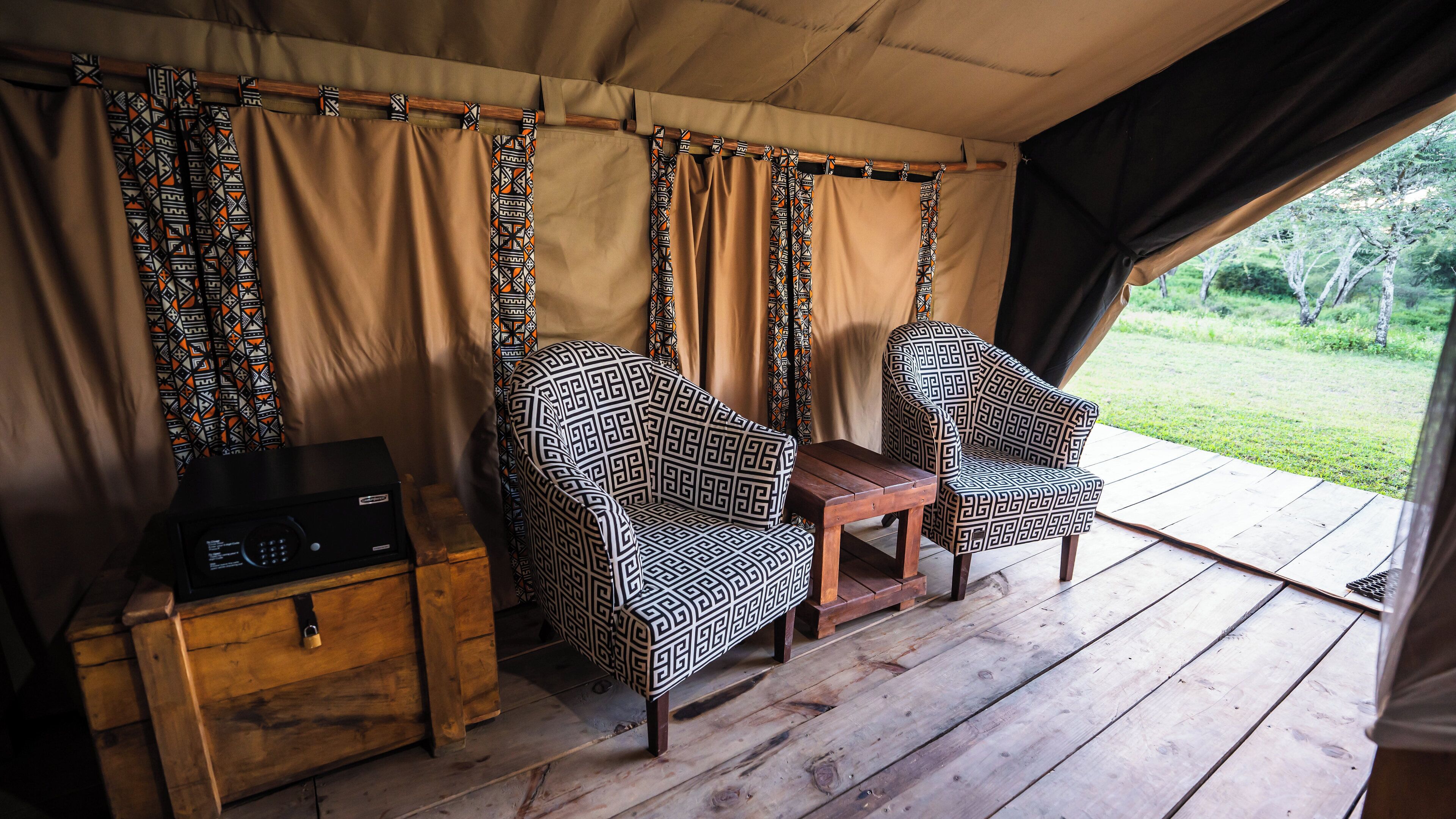 Een tent met twee gestreepte stoelen, een klein houten tafeltje en een radio op een dressoir.