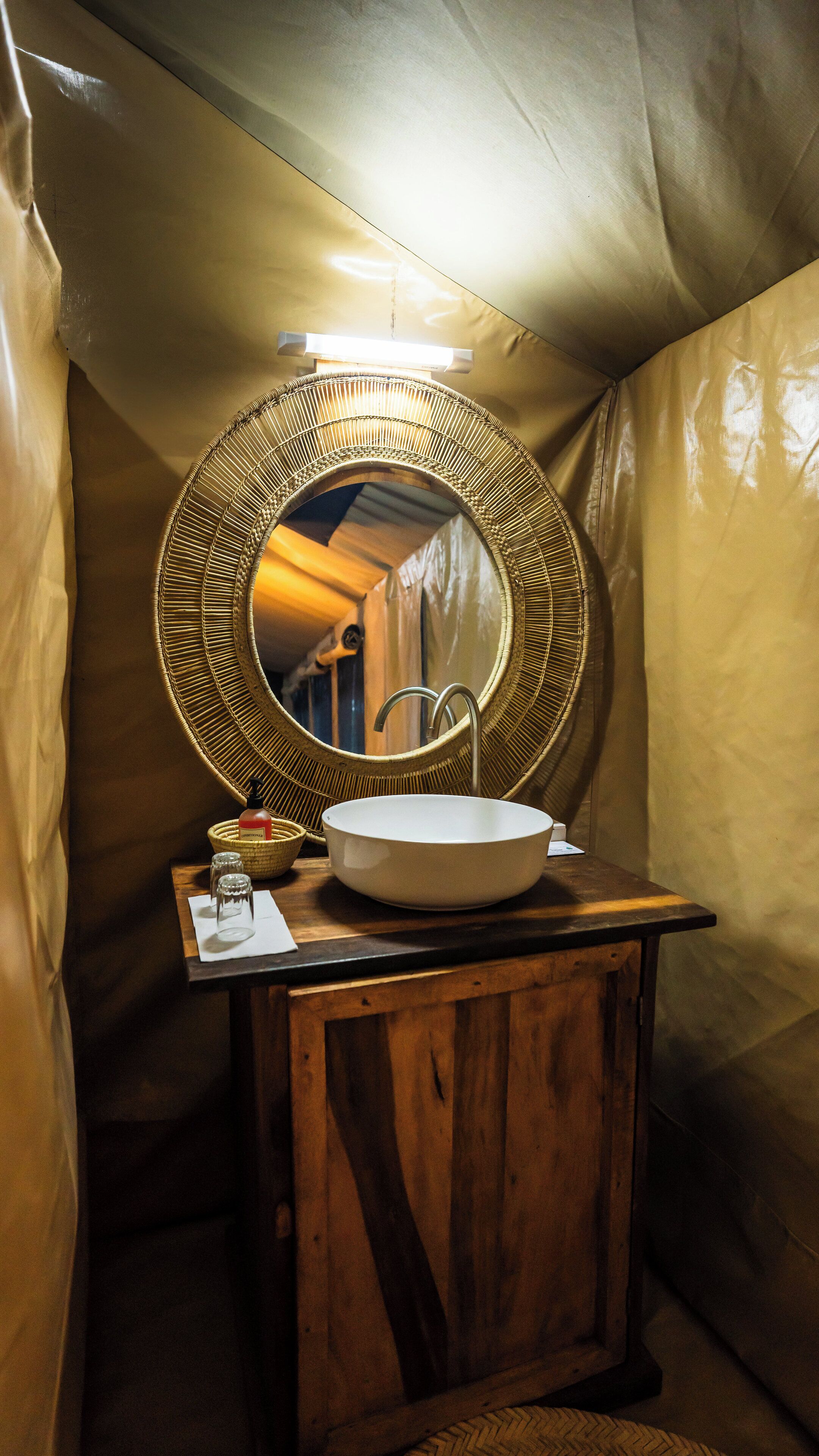 A compact bathroom with a round mirror, a white sink, and a small bottle of soap.