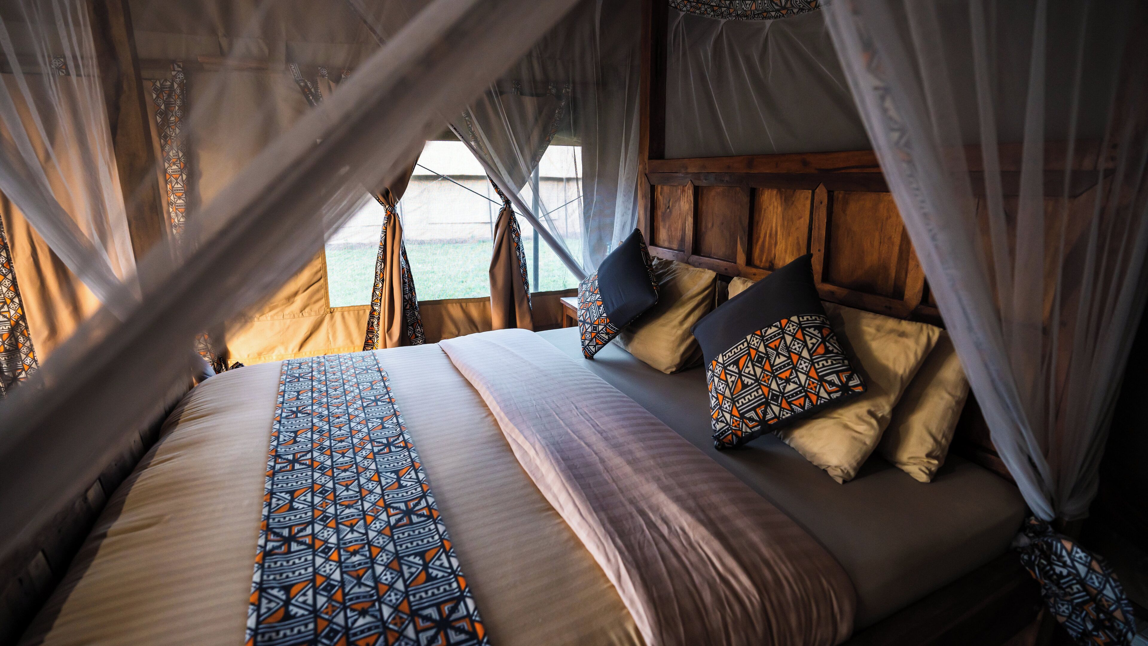 A bed with patterned pillows and a canopy, a wooden headboard, and a view through the window.