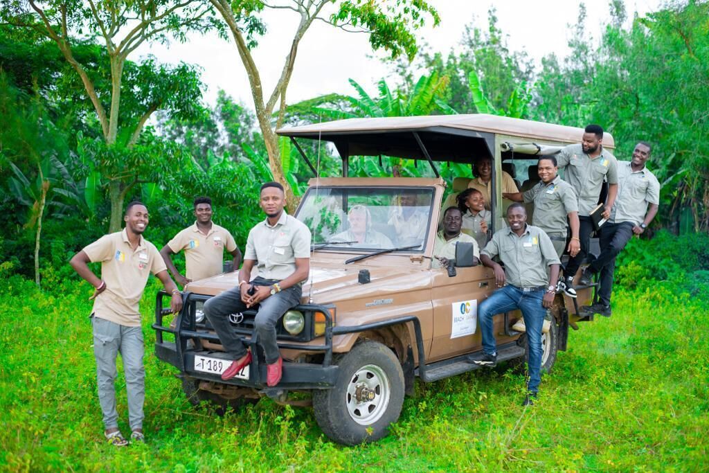 Un grupo de personas vestidas para un safari cerca de un vehículo todoterreno marrón en un entorno verde y exuberante.