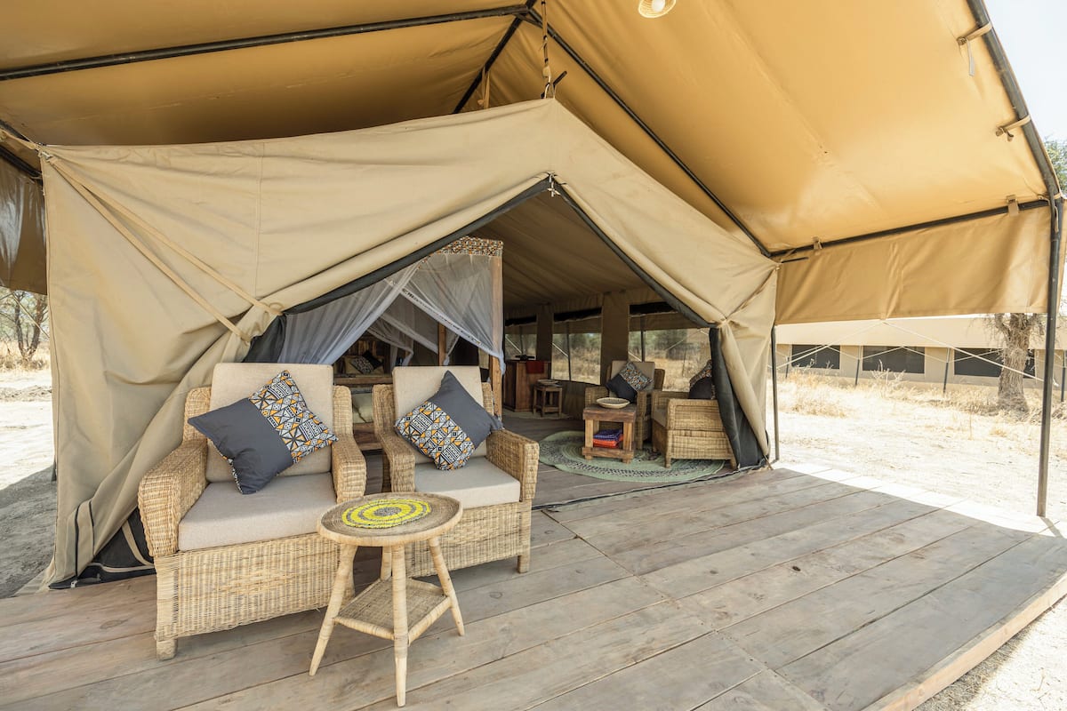 Een tent met een rieten bank en een kleine tafel, omringd door een houten terras.