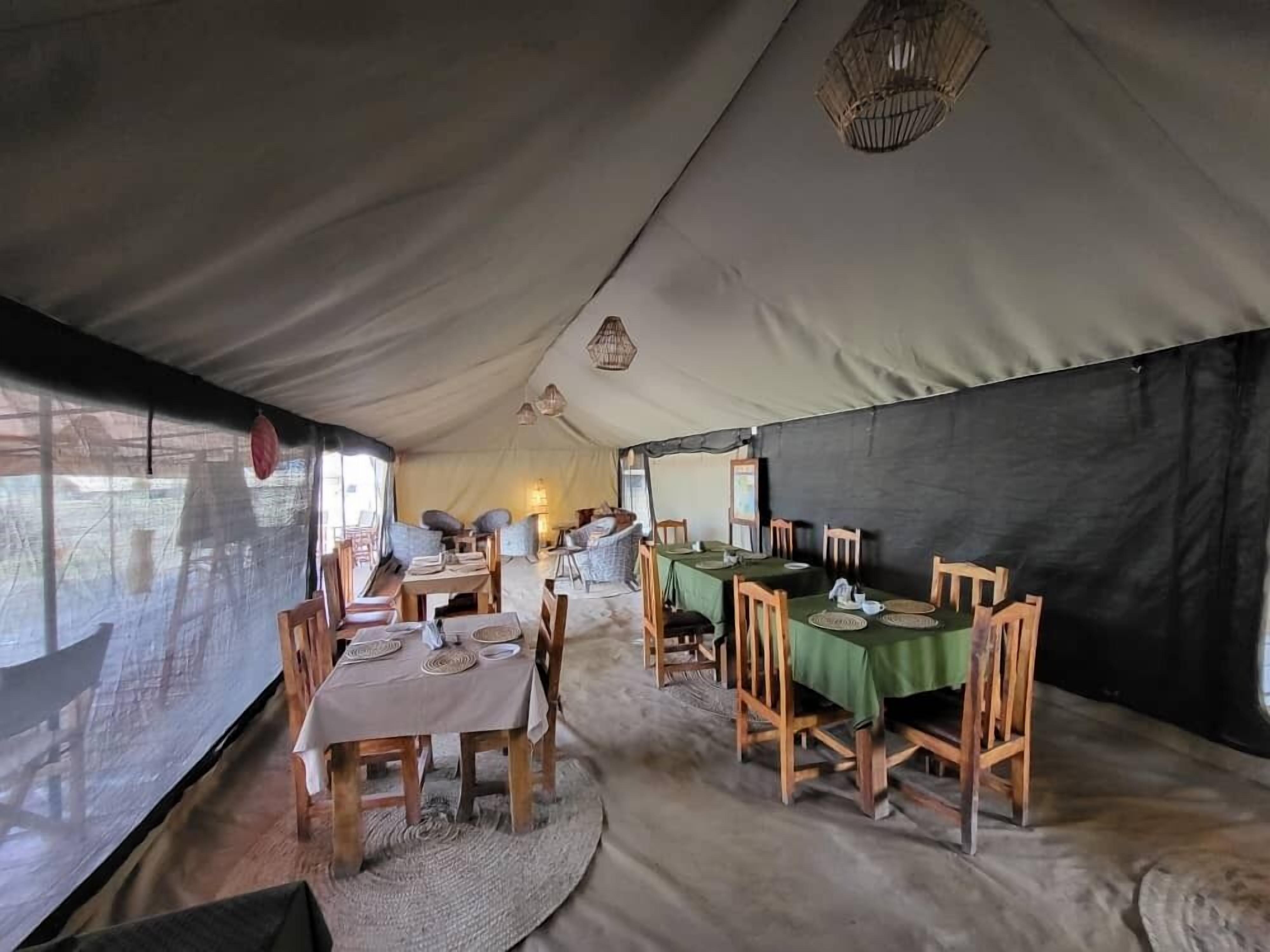 A tented dining area with tables and chairs, a woven rug, and a hanging light fixture.