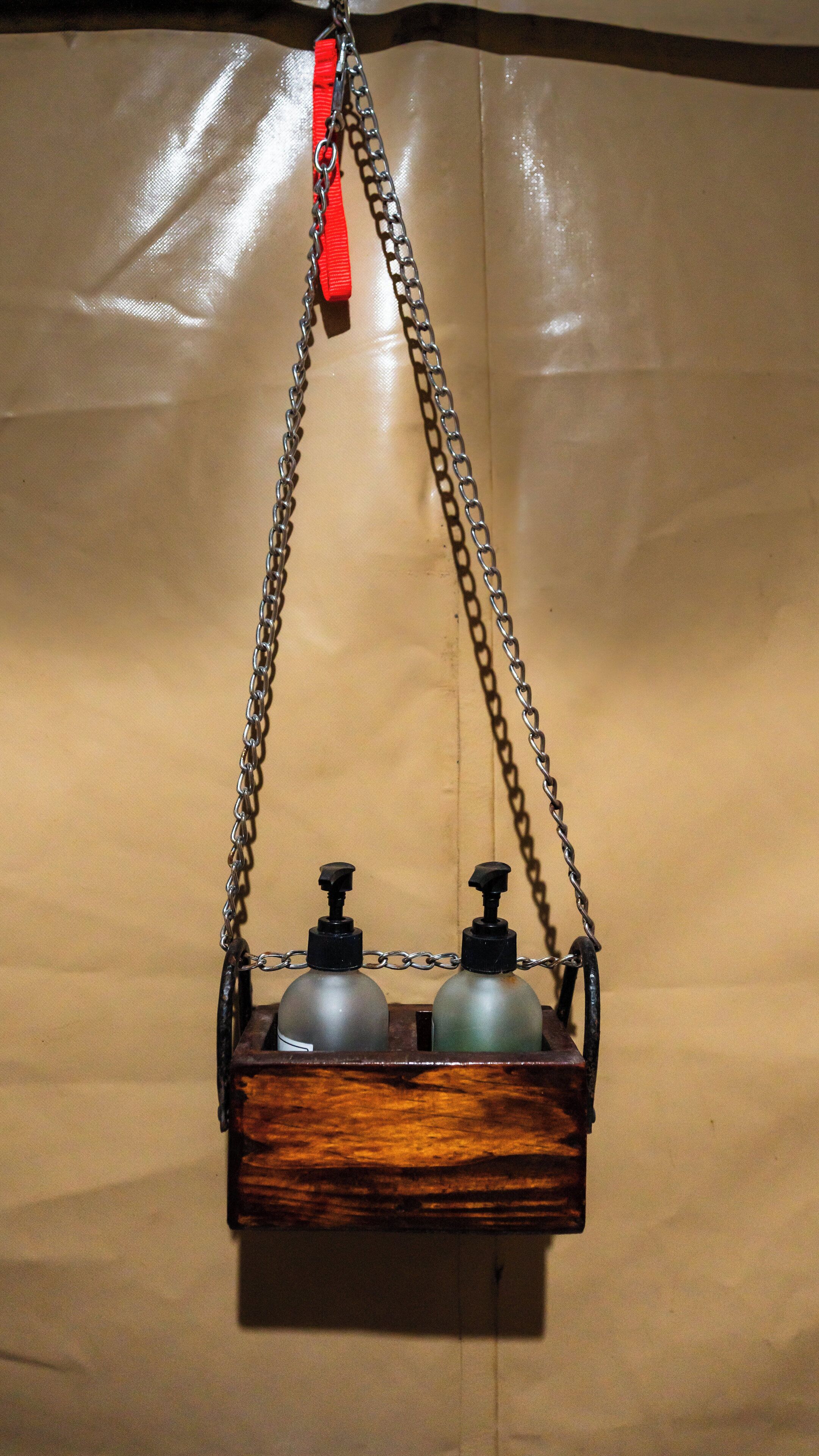 A wooden chest with two bottles and a pump, suspended by chains.
