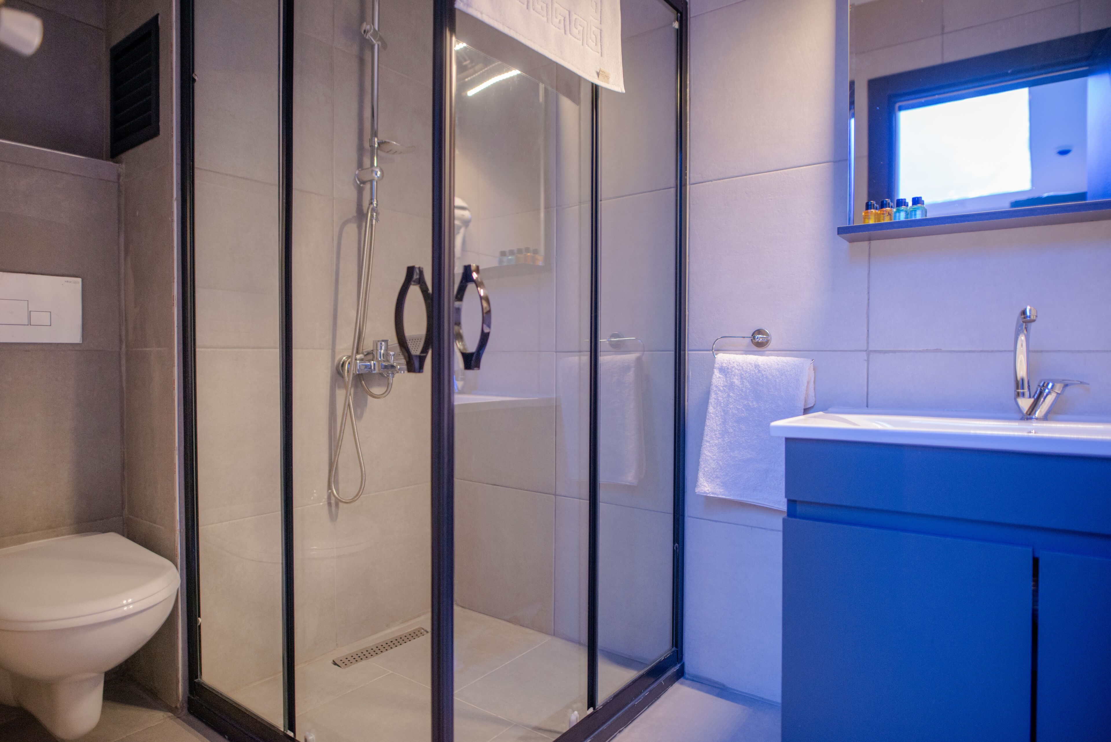 Un baño moderno con ducha envuelta en vidrio, inodoro blanco y tocador azul con espejo.