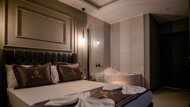A hotel room with a large bed, a bathroom with a glass shower, and a minibar. - Zara Suit (Istanbul)