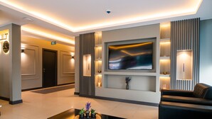 A modern lobby with a flat-screen TV, a coffee table with decorative items, and a seating area with a sofa. - Zara Suit (Istanbul)