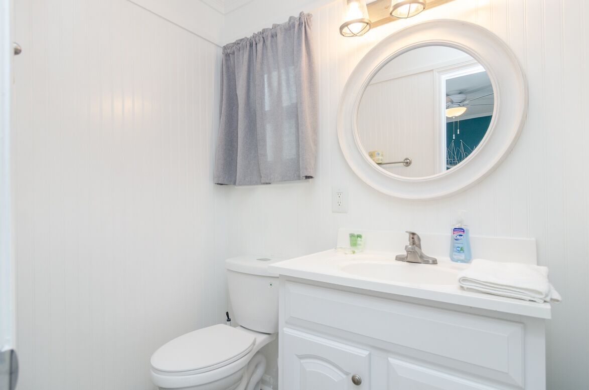 A bathroom with a white toilet, a round mirror, a vanity with a sink, and a towel on the counter.
