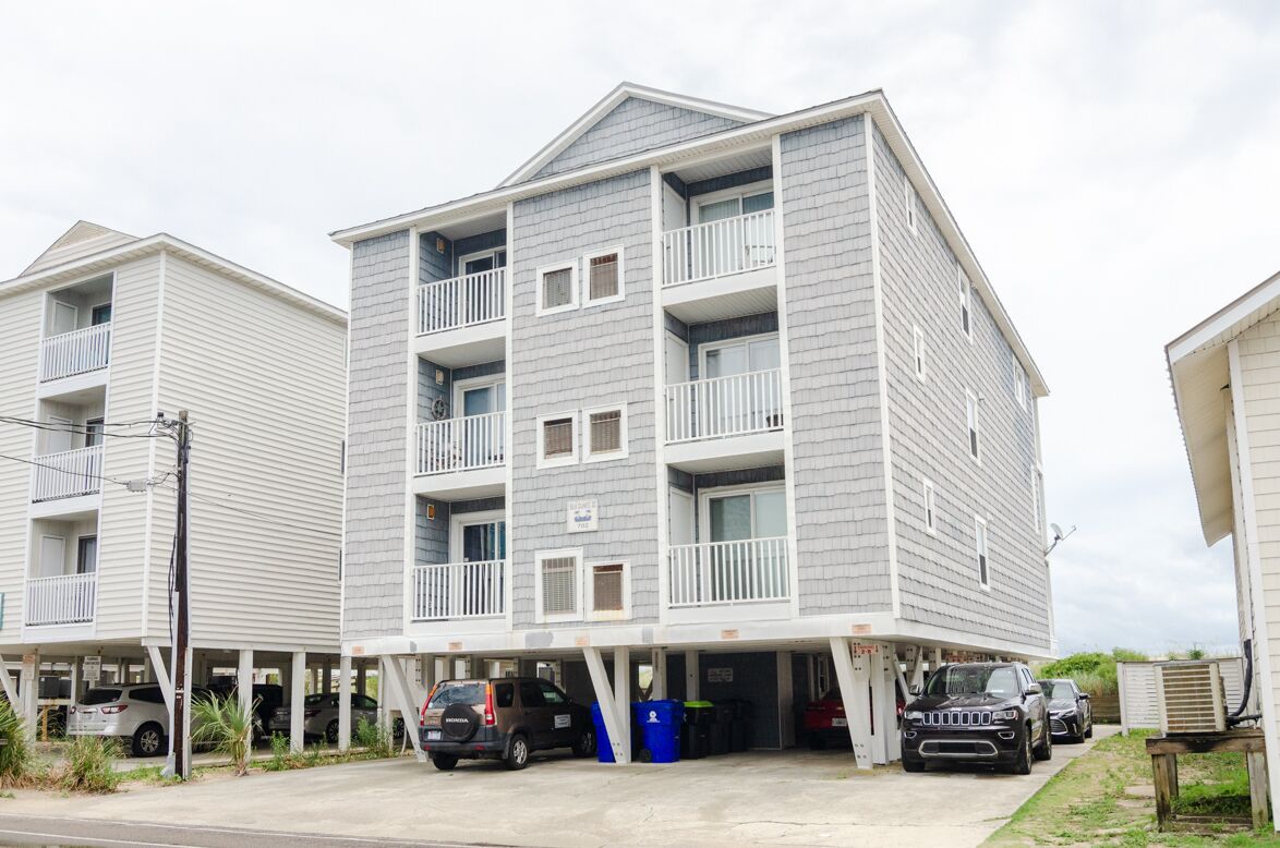 A multi-story residential building with balconies, parking spaces, and a gated entrance.