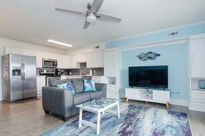 A modern kitchen with white cabinets, stainless steel appliances, and a grey sofa. - Stunning 2 bedroom beachfront oasis! (Carolina Beach)