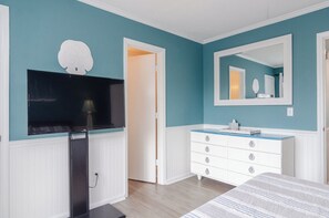 A bedroom with teal walls, a white dresser, a large mirror, and a flat-screen TV mounted on the wall. - Stunning 2 bedroom beachfront oasis! (Carolina Beach)