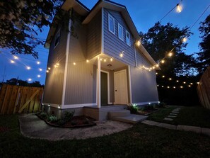 A two-story house with a front porch, a wooden fence, and string lights. - Spacious 1 bedroom Avondale guesthouse 🏡 (Jacksonville)