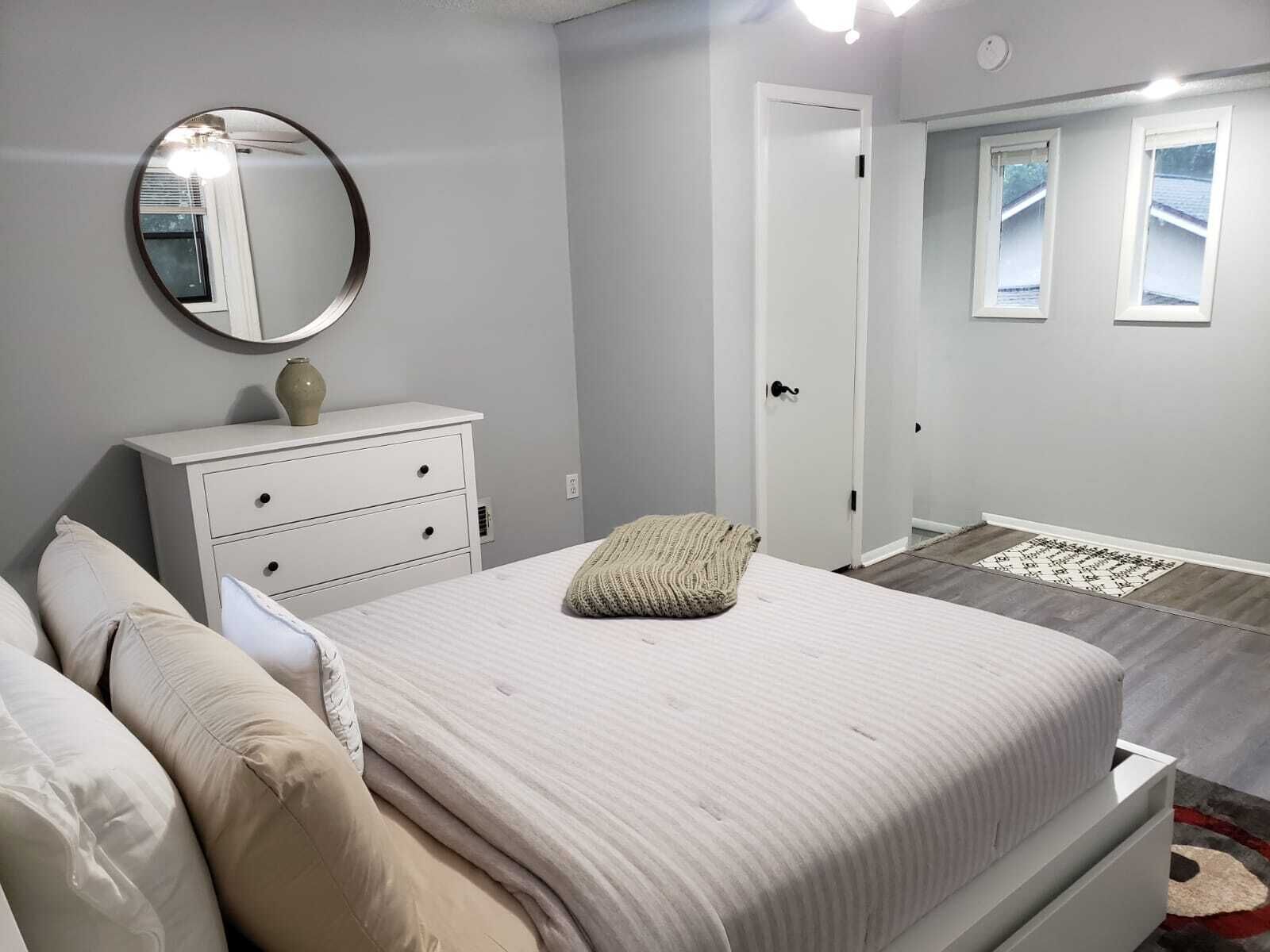A bedroom with a bed, a dresser, a mirror, and a door leading to another room.