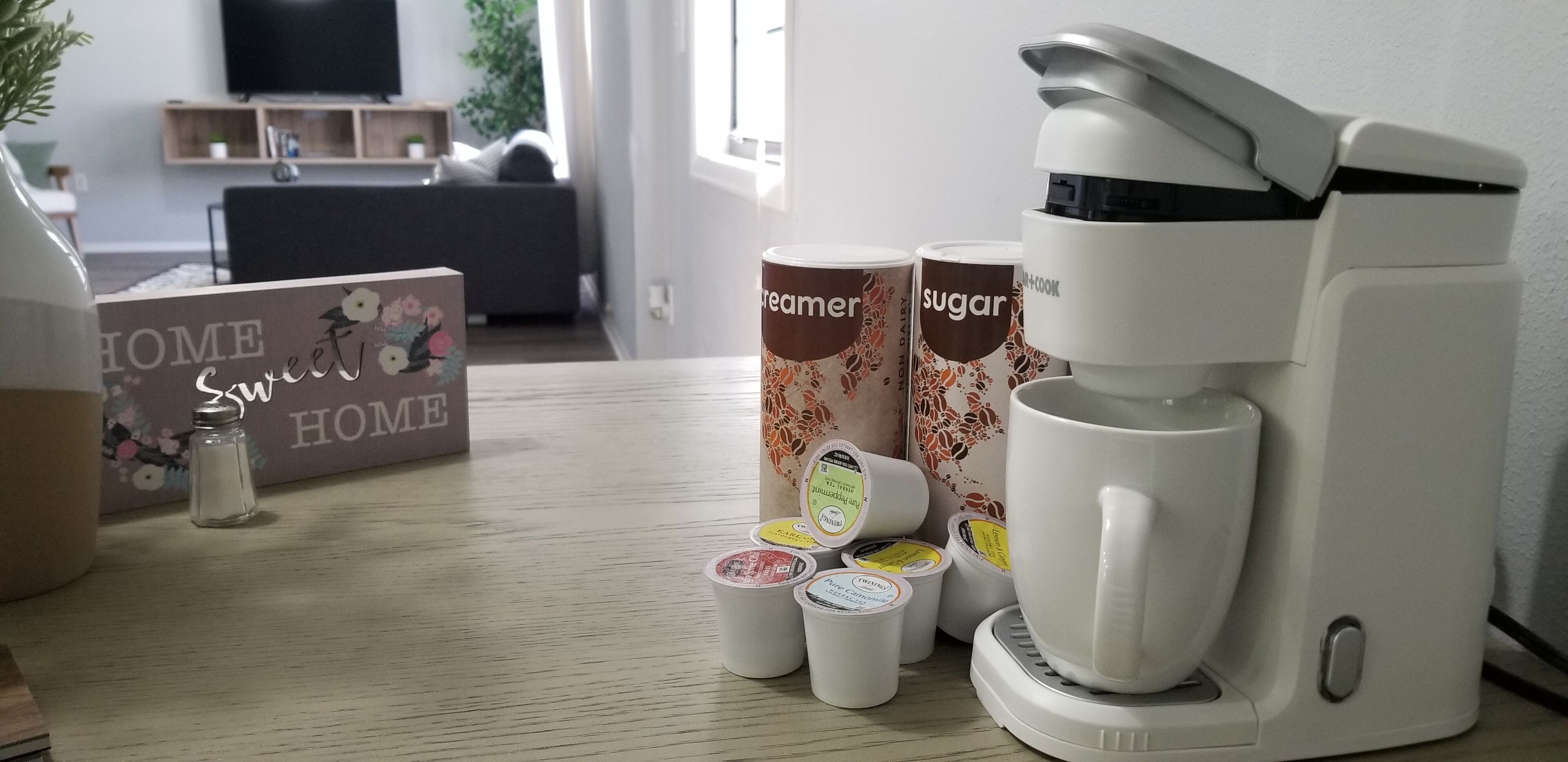 Eine Kaffeemaschine, Zuckerportionen und Sahnebecher auf einem Holztisch.