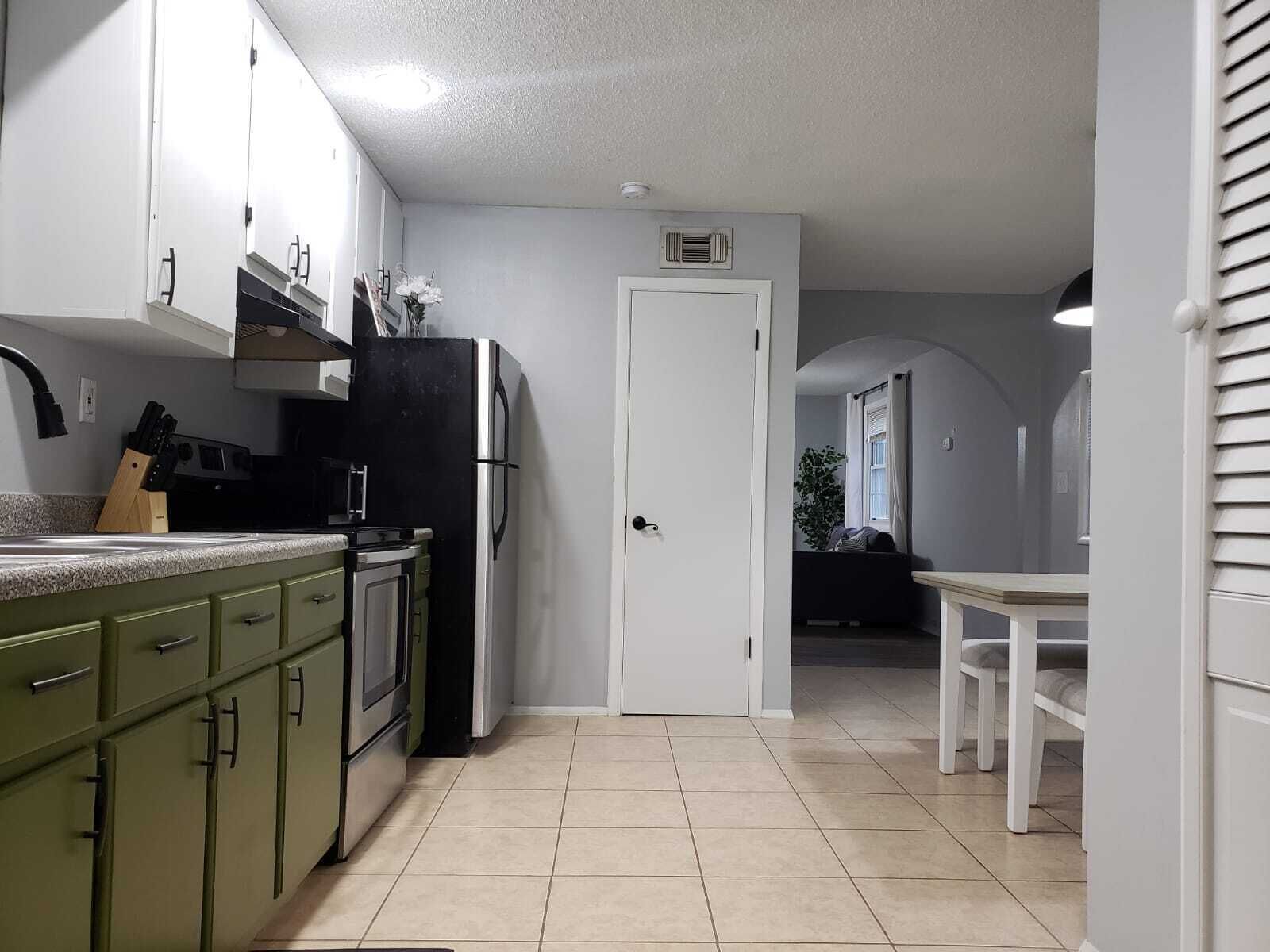 A kitchen with green cabinets, a black refrigerator, and a white door leading to another room.