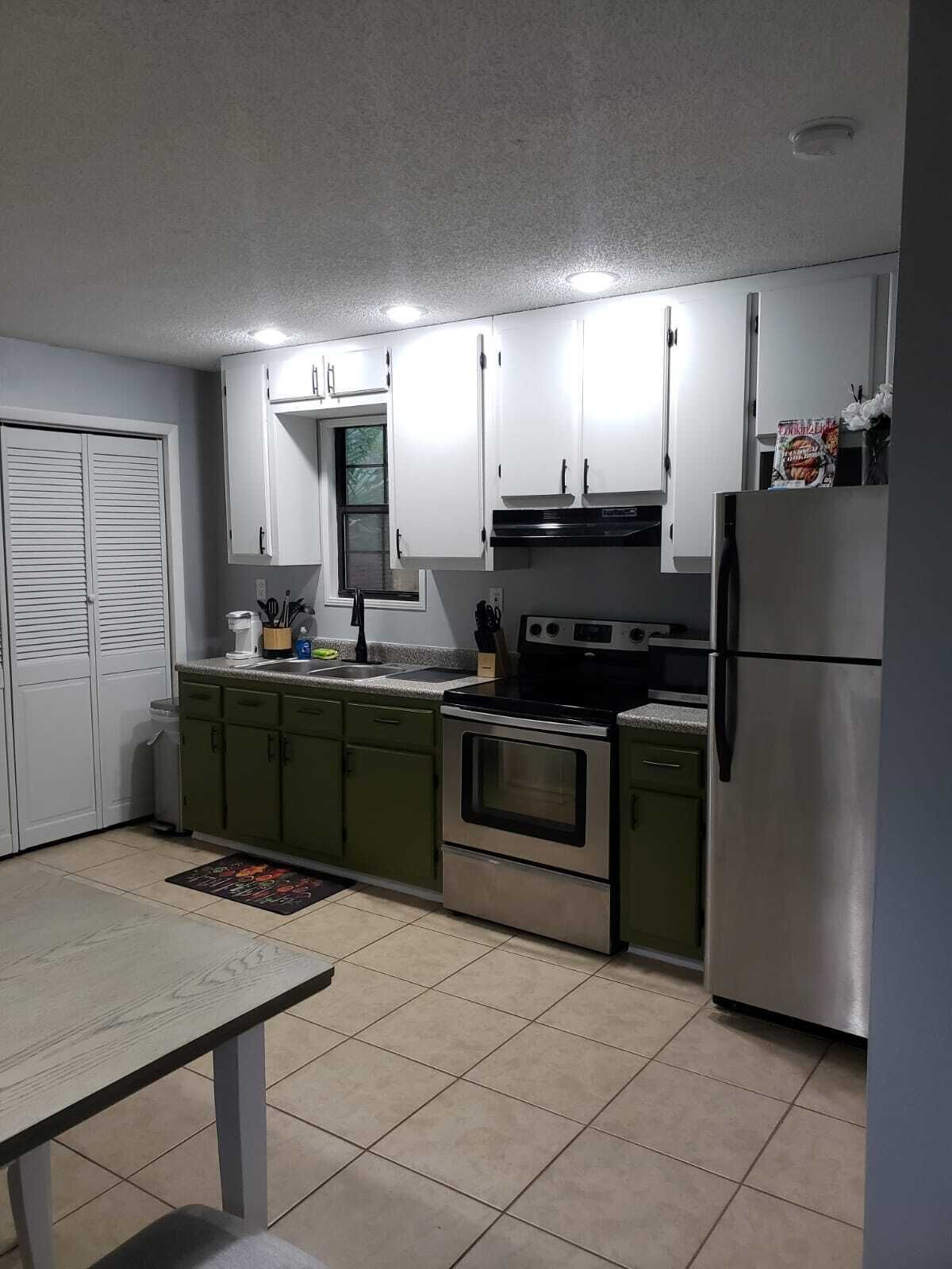 A compact kitchen with white cabinets, a stainless steel refrigerator, an oven, and a sink.