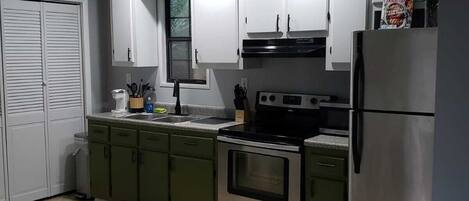 A compact kitchen with white cabinets, a stainless steel refrigerator, an oven, and a sink.