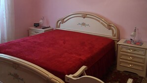 A bedroom with a bed, bedside tables, a chair, a nightstand, a lamp, a wall decoration, and a chandelier.