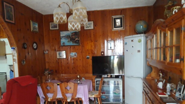 A wooden-paneled room with a dining table, chairs, a television, and a refrigerator.