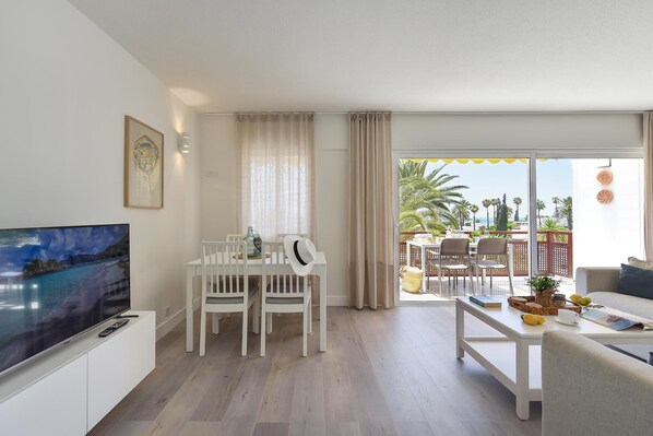 Un salon moderne doté d’un téléviseur à écran plat, d’une table à manger avec des chaises et d’un balcon aménagé avec du mobilier d’extérieur.