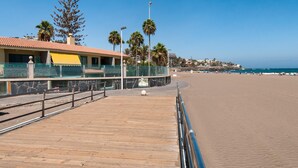 A wooden boardwalk leading to a beach with a building featuring a yellow awning and a stone facade.