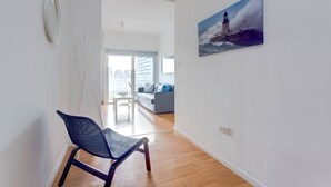 Un salon moderne avec une grande fenêtre, un tableau représentant un phare et un fauteuil bleu.