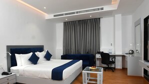 A modern hotel room with a large bed, a desk, a chair, and a small table with fruit. - Kyriad Hotel Pimpri (Pune)