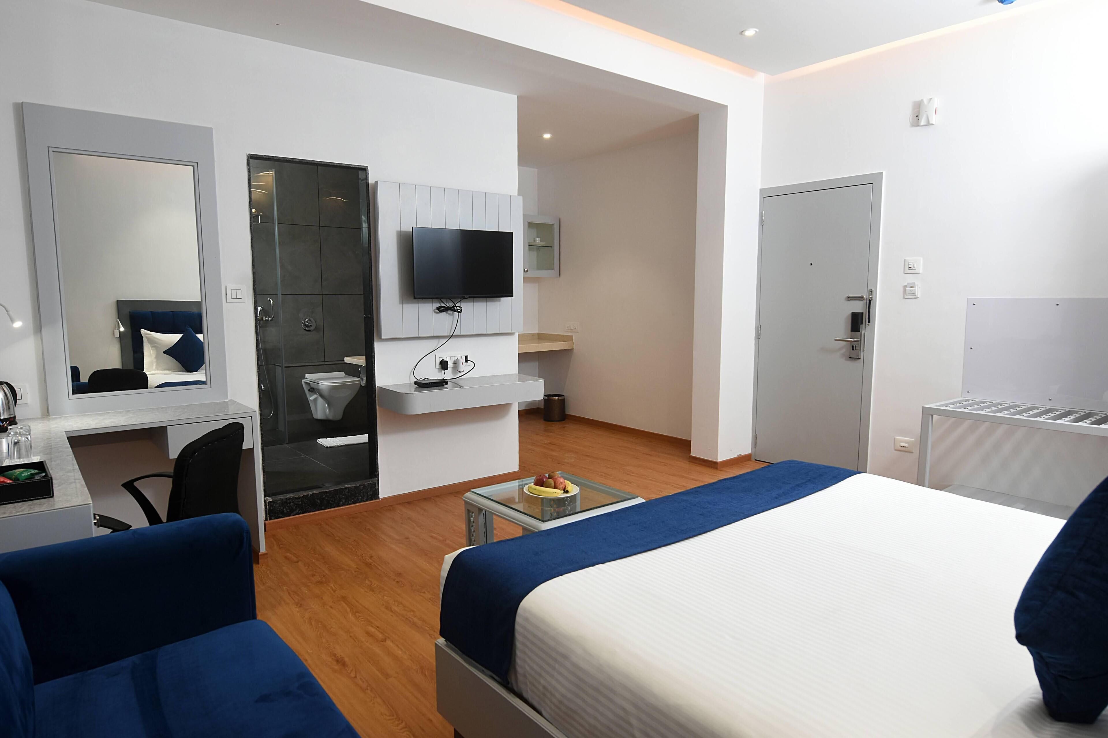 A modern hotel room with a bed, a desk, a chair, a TV, and a bathroom.