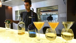 A bar area with a bartender pouring a drink, a bottle of whiskey, and several glasses on the counter. - Kyriad Hotel Pimpri (Pune)