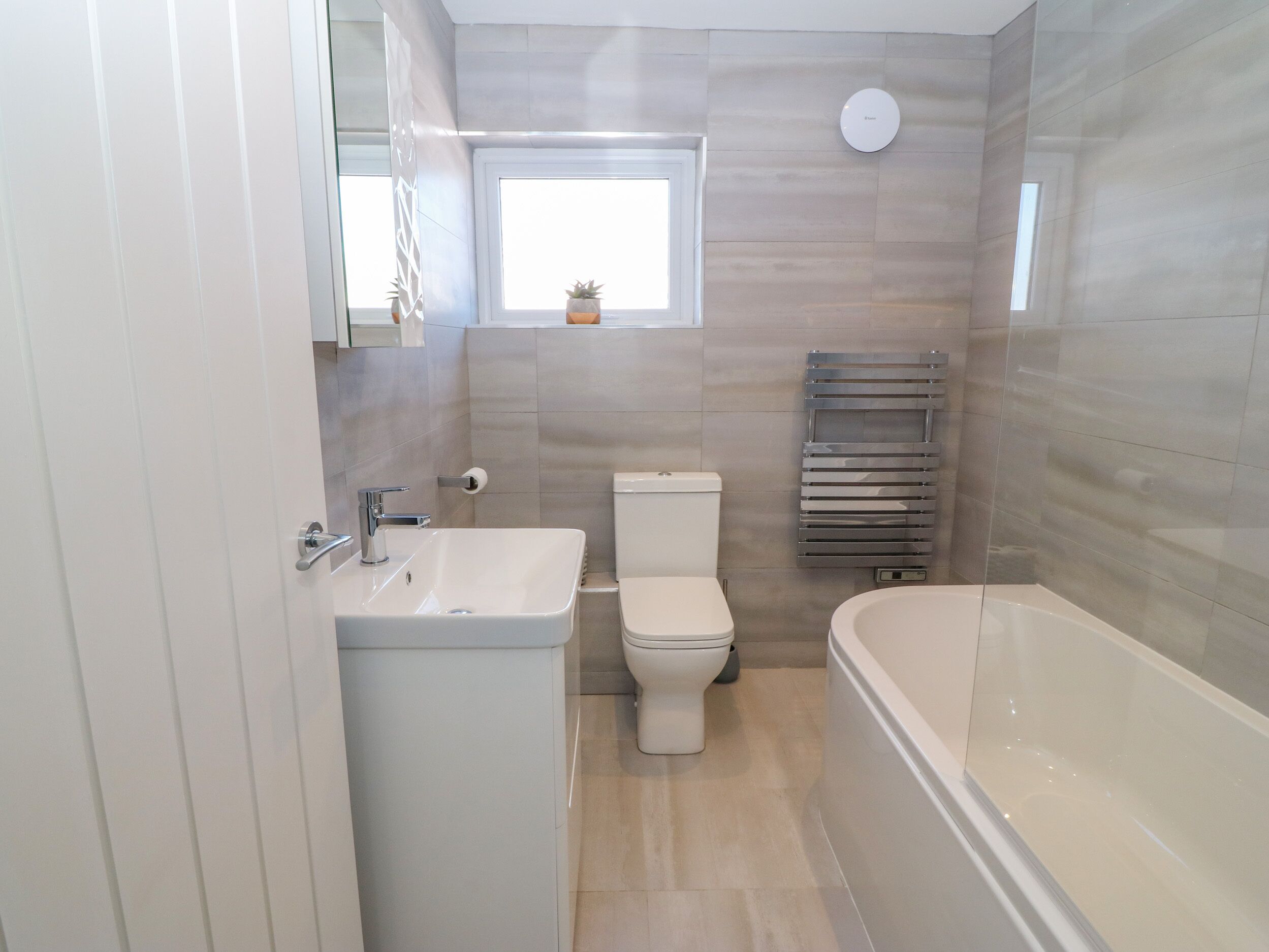 A modern bathroom with a sink, toilet, and bathtub. There is a window above the toilet and a towel rack on the wall.