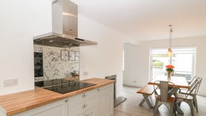 A modern kitchen with a wooden countertop, stainless steel range hood, and a dining area with a wooden table and metal chairs. - Daresfield (Cemaes Bay)
