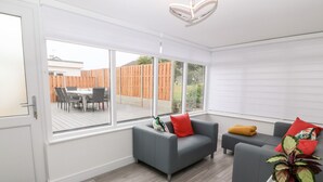A modern living room with grey sofas, a wooden deck visible through large windows, and a white ceiling light. - Daresfield (Cemaes Bay)