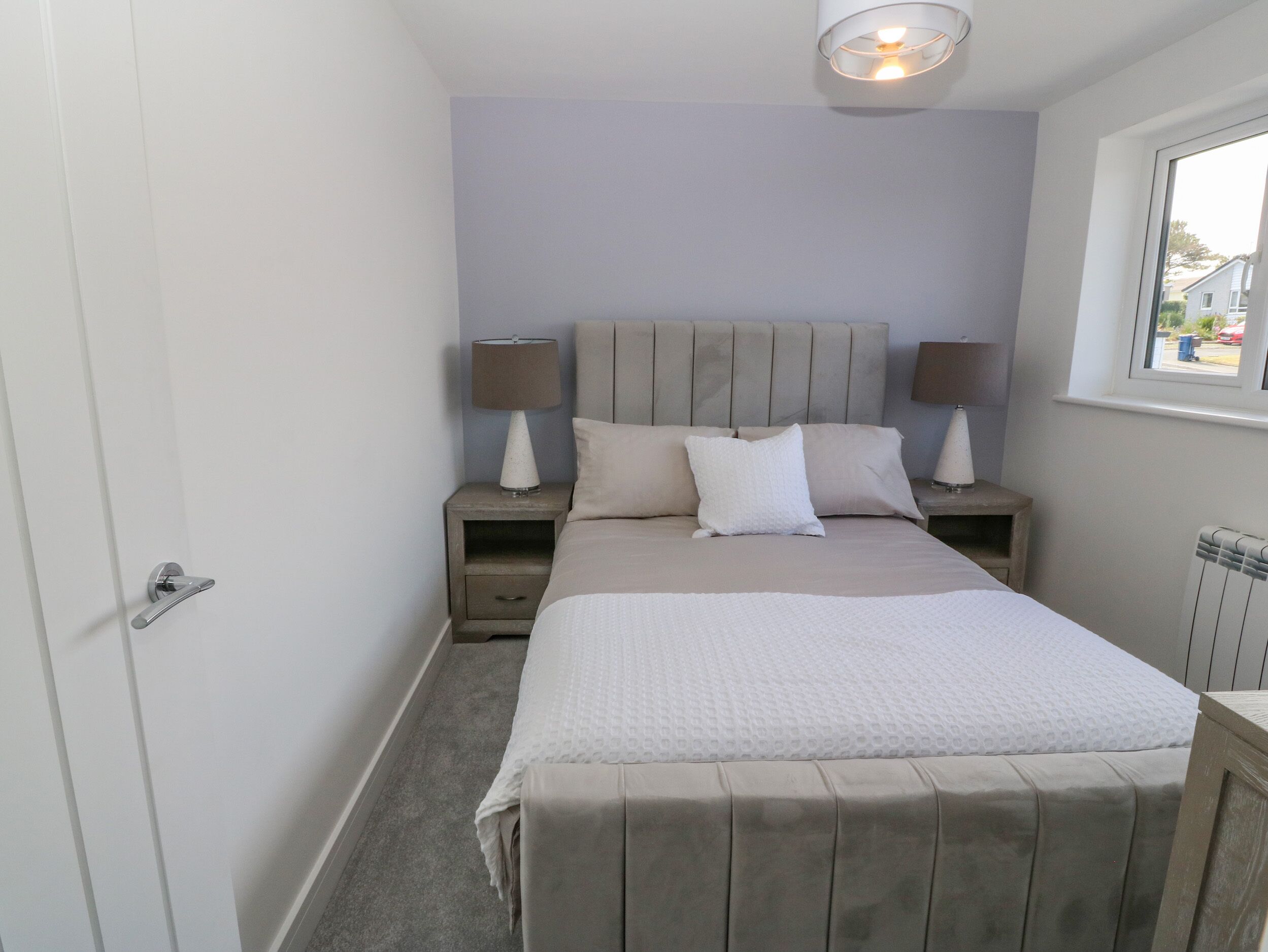 A bedroom with a bed, two bedside tables with lamps, a window, and a radiator.