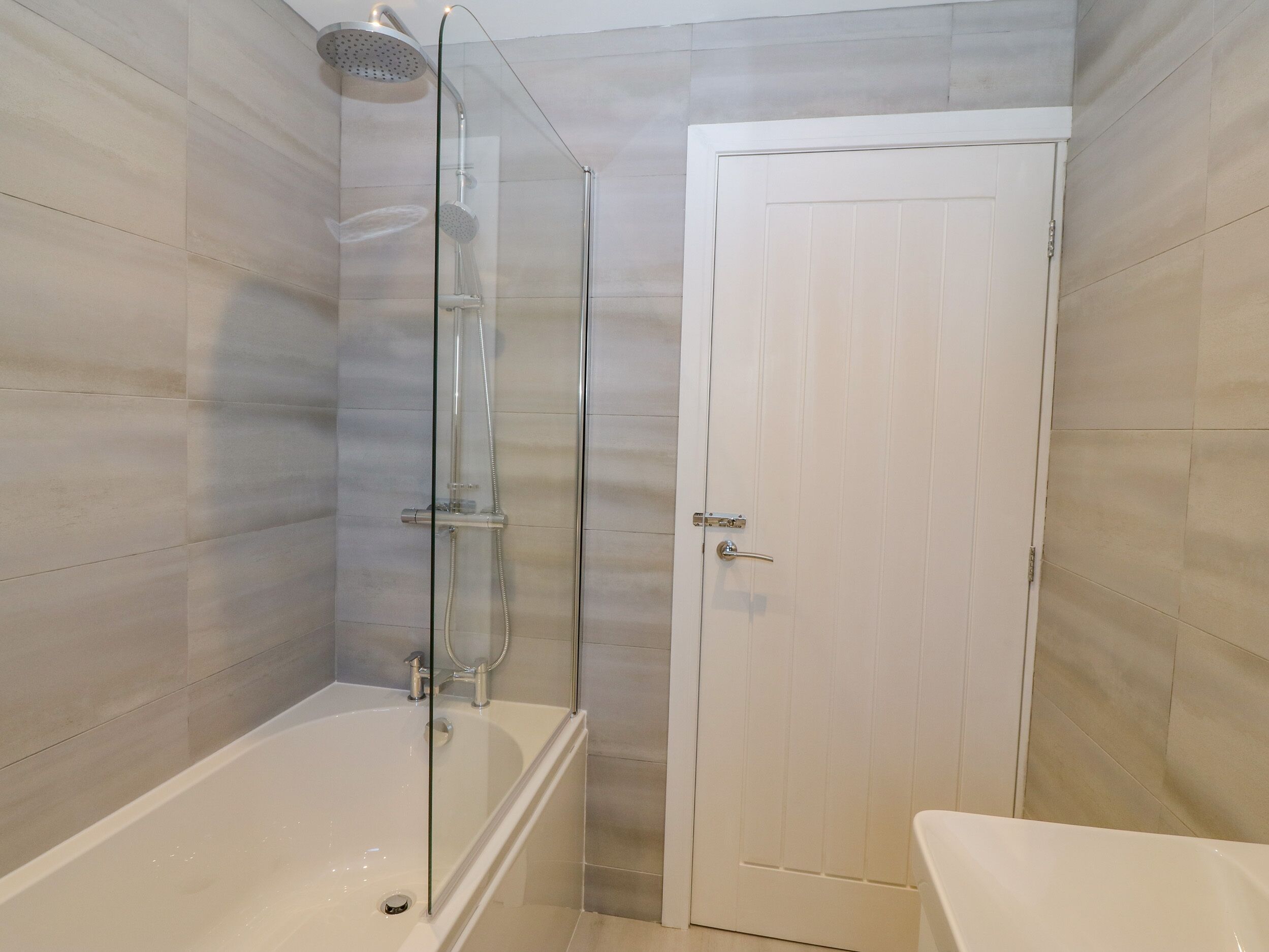 A bathroom with a glass-enclosed shower, a white bathtub, and a white door.