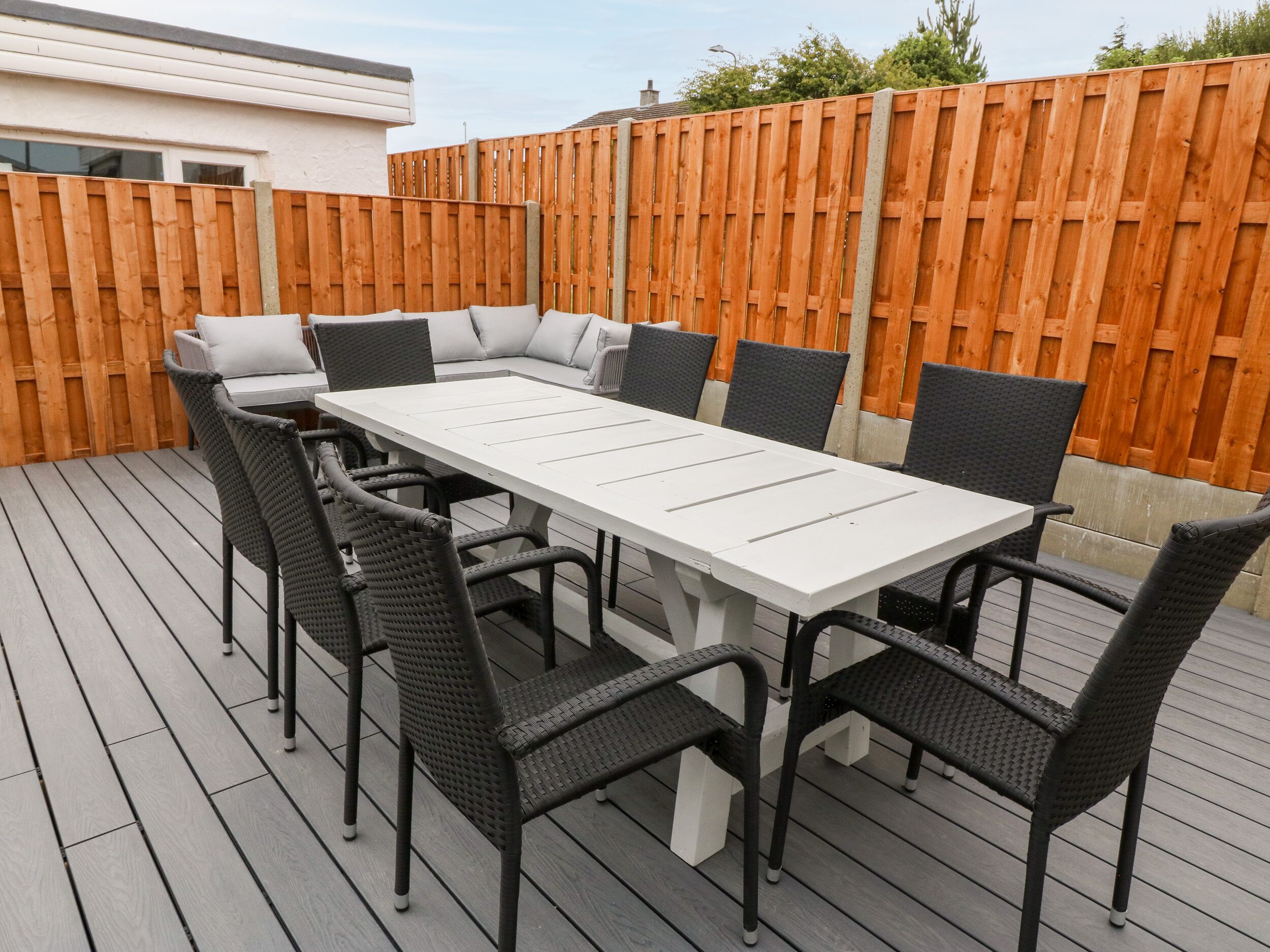 A rectangular outdoor dining table with six chairs, surrounded by a wooden deck.