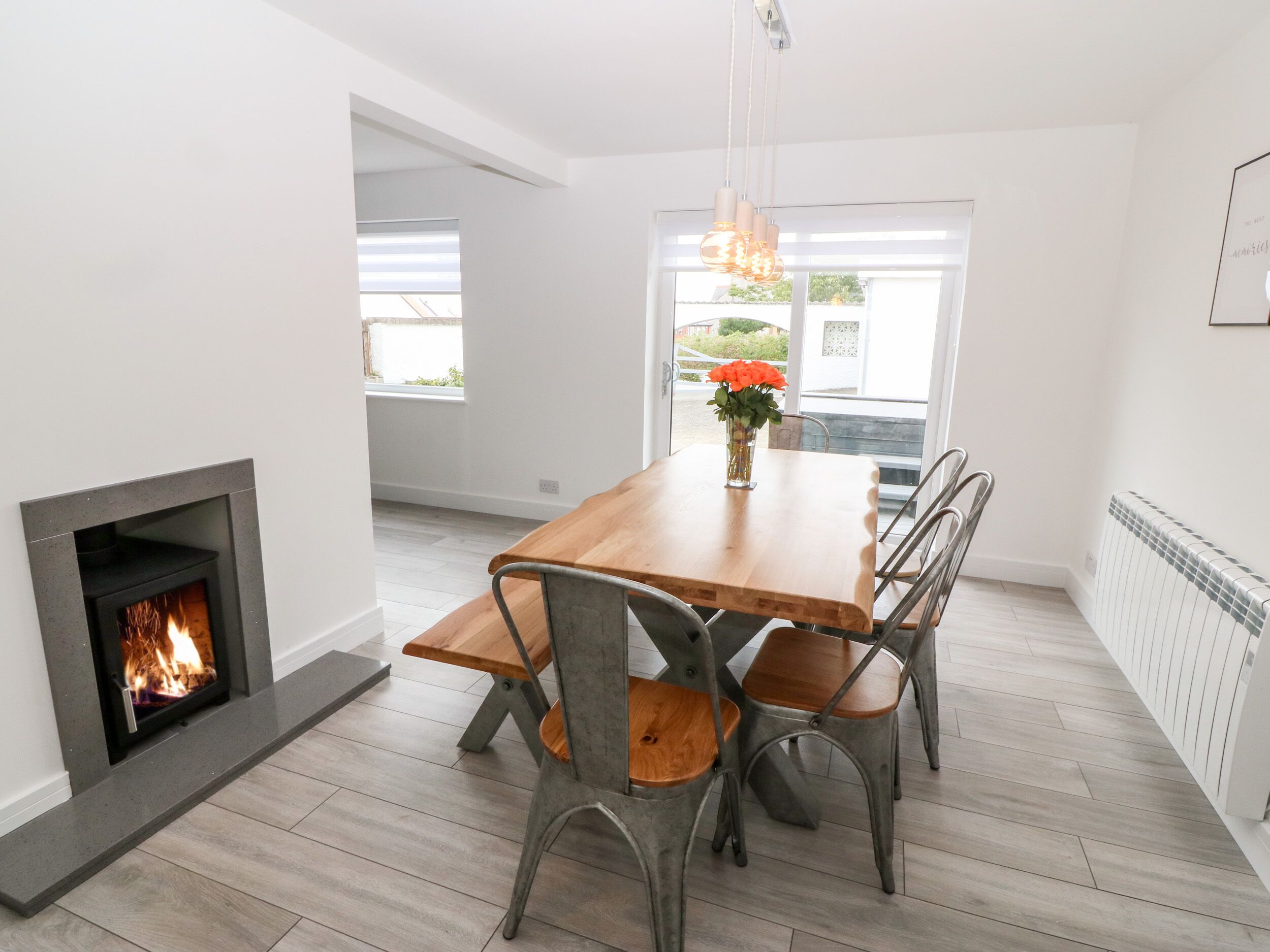 Comedor con chimenea, mesa de madera, sillas de metal y vistas al exterior.