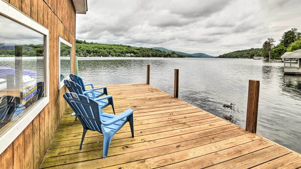 A wooden deck with blue chairs and a glass window overlooking a lake. - Lakefront Alton Bay Retreat w/ Dock Near Beaches! (Alton Bay)