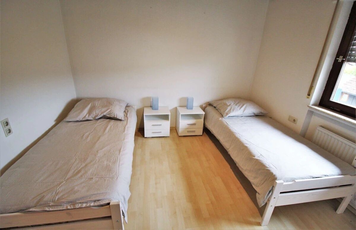 A small, single-room with two single beds, each with a nightstand and a drawer.