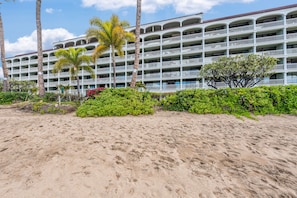 A beachfront hotel with multiple balconies, palm trees, and a sandy beach.