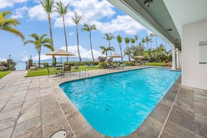 A swimming pool with a tiled deck, palm trees, and a view of the ocean.