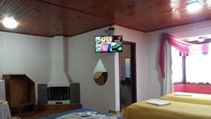 A hotel room with two beds, a TV mounted on the wall, a fireplace, and a window with curtains. - Pousada Por do Sol (Camanducaia)