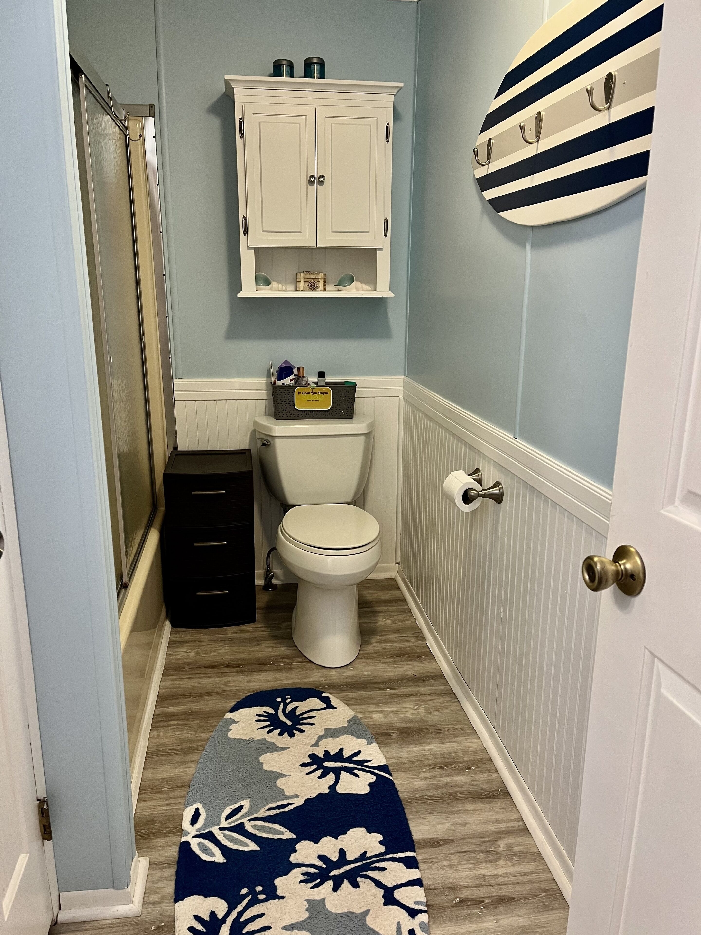 Une salle de bain comprenant des toilettes, un meuble au-dessus des toilettes, une douche et une porte dotée d’une poignée.