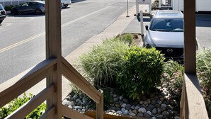 Vista da un balcone in legno su una strada con auto e un edificio con balconi.