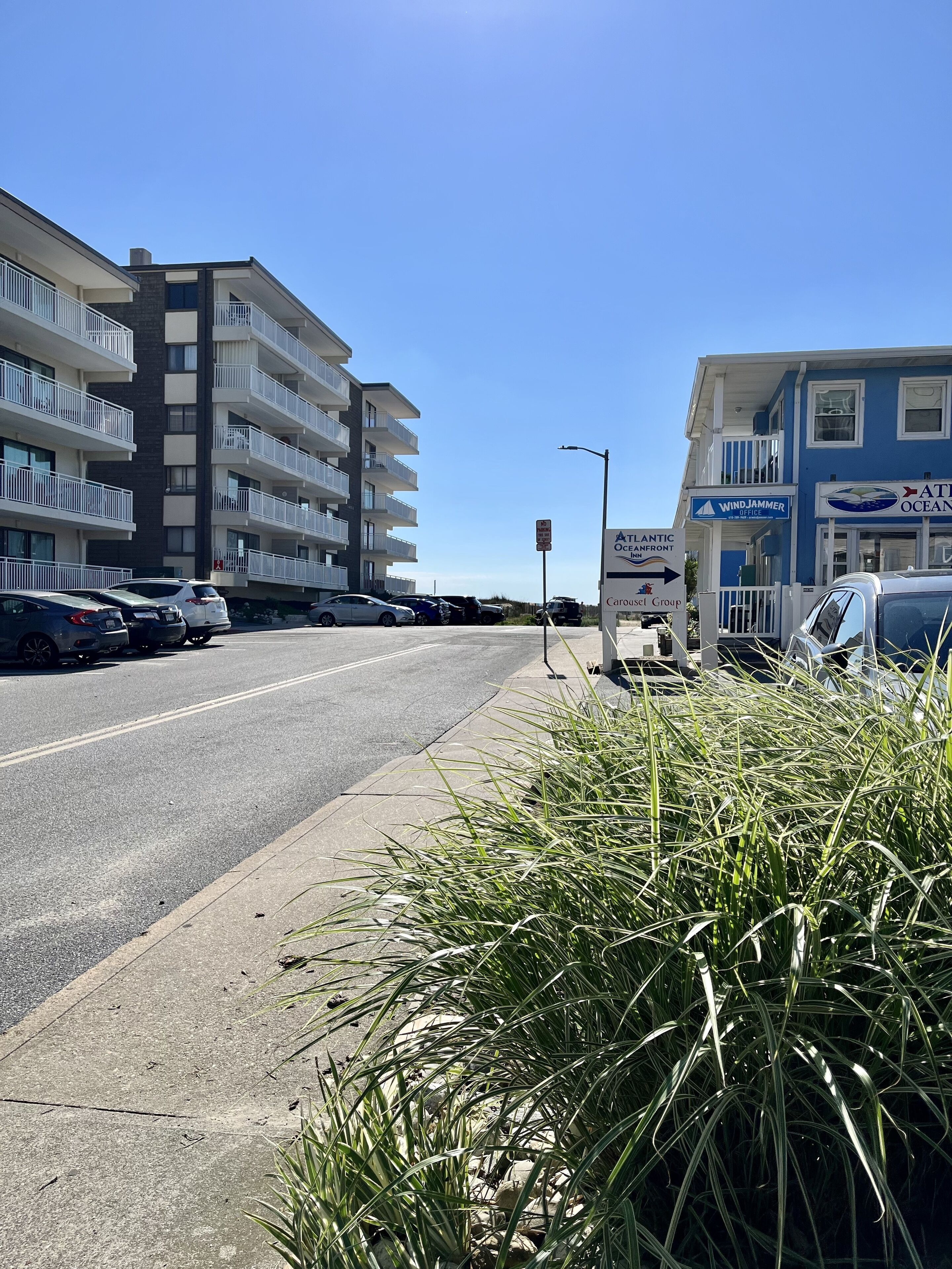 A coastal road with a multi-story building featuring balconies, a sign for Atlantic Oceanfront Inn, and parked cars.