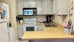 Una cucina con mobili bianchi, un forno a microonde, un fornello, un lavello e due sgabelli di legno.