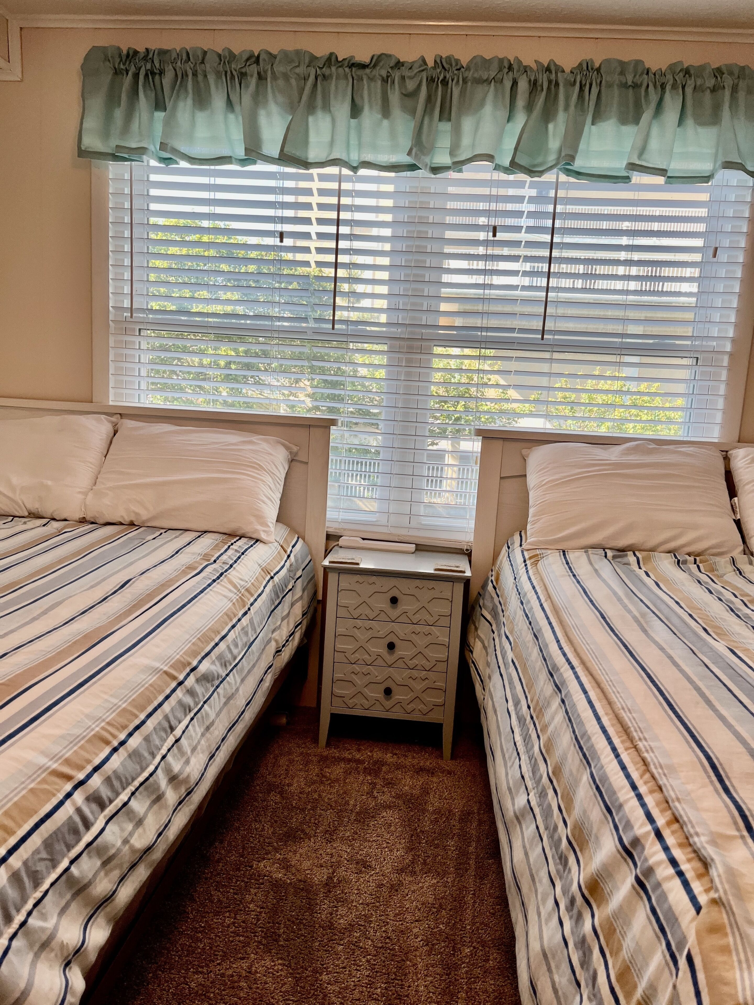 A room with two beds, a nightstand, and a window with blinds.