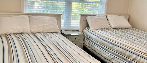 A bedroom with two beds, a ceiling fan, a window with blinds, and a nightstand.