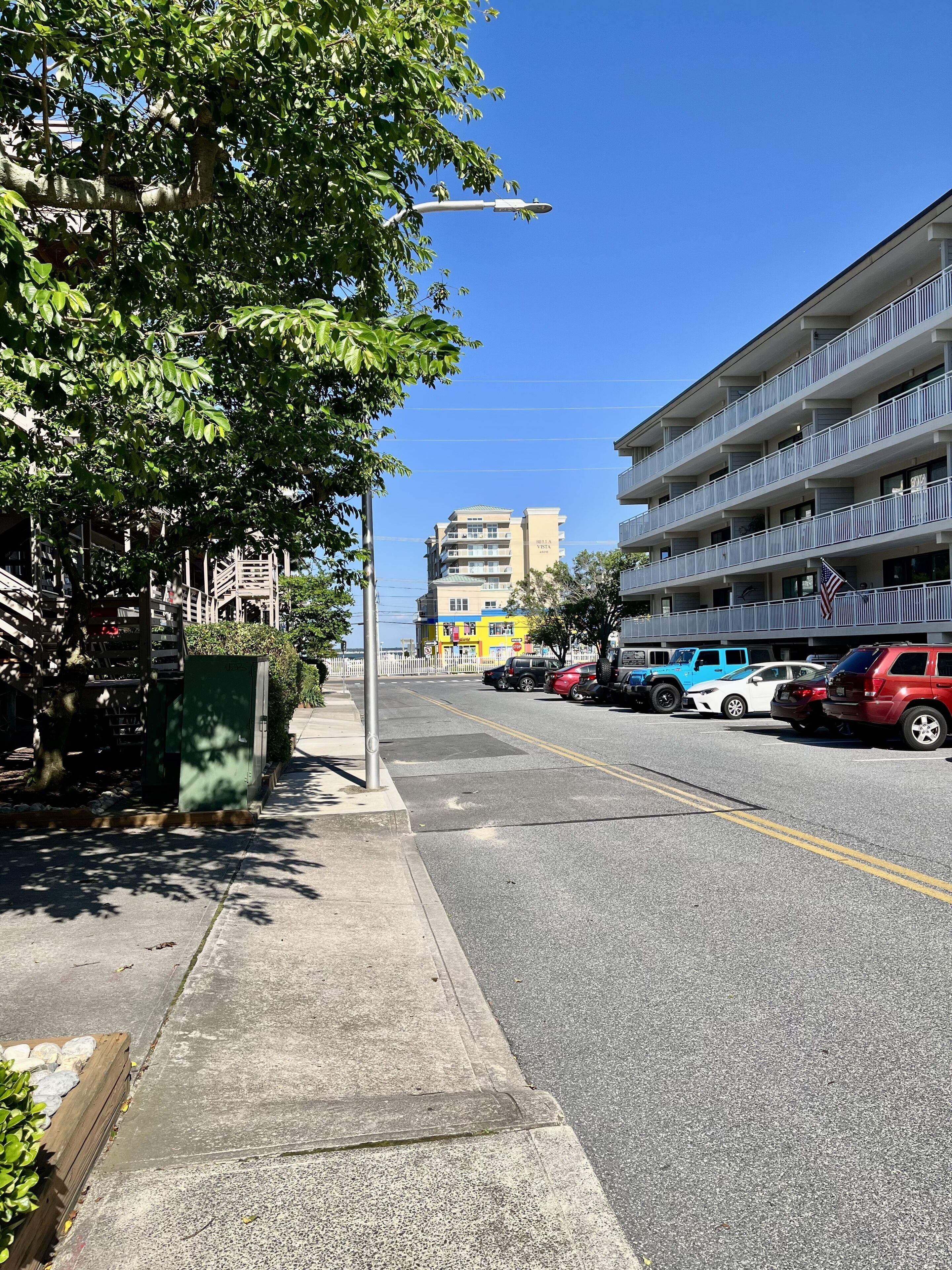 A multi-story hotel with balconies and a parking lot with several cars.