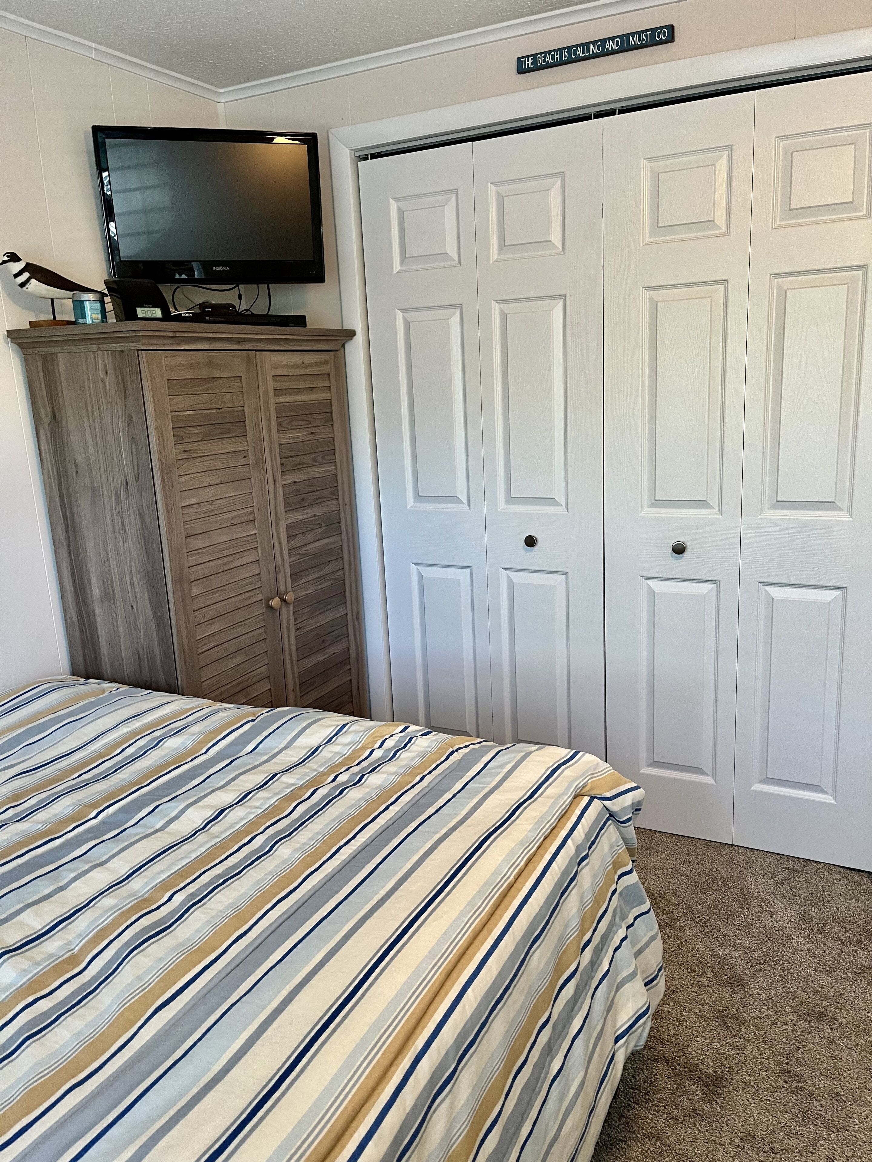 A bedroom with a bed, a television on a wooden cabinet, and a white door with a sign above it.